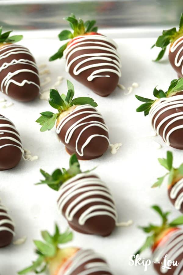 Sheet pan with 8 chocolate covered strawberries drizzled with white chocolate, by Skip to my Lou.