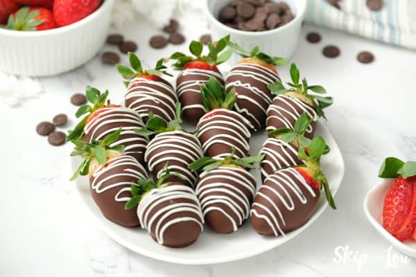 12 chocolate covered strawberries, drizzled with white chocolate, arranged on a white serving plate, by Skip to my Lou.