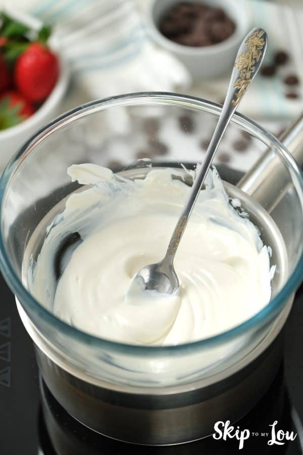 Silver spoon sticking out of a glass bowl with melted white chocolate, by Skip to my Lou.
