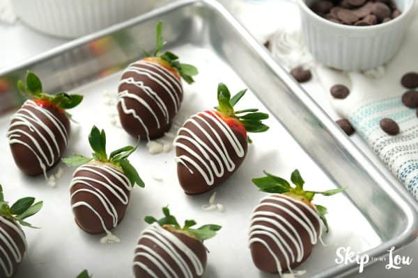 6 Chocolate covered strawberries drizzled with white chocolate sitting on a lined sheet pan, by Skip to my Lou.