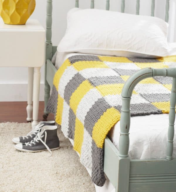 Yellow white and gray patchwork blanket on top of a bed.