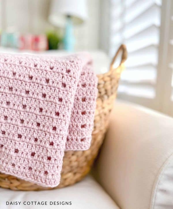 Pink crochet blanket laid over a pillow. 