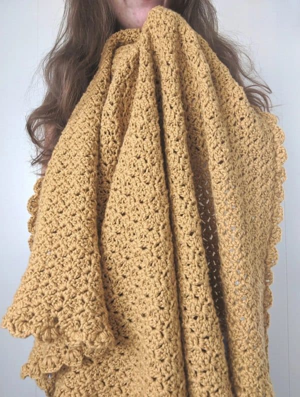 Woman holding a brown crochet blanket.
