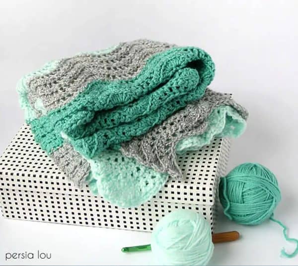 Gray and green blanket next to balls of yarn.