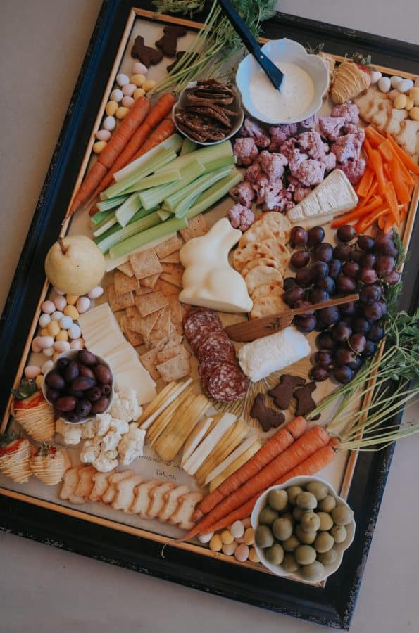 A traditional Easter charcuterie board idea from nesting with grace that includes crackers, veggies, dip, and some chocolate bunnies.
