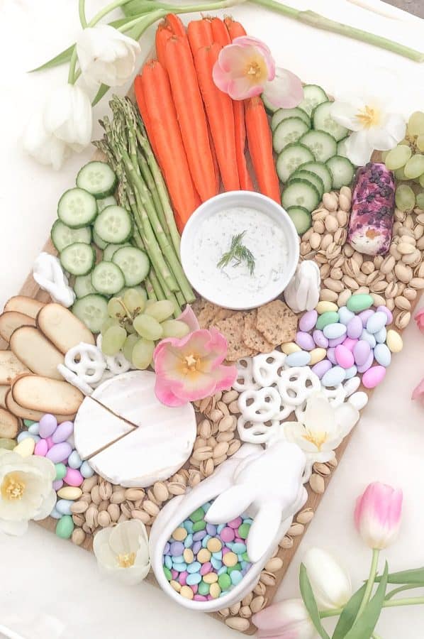 A pastel colored Easter charcuterie board idea from diary of a debutante with veggies, nuts, cheese, and sweet desserts.