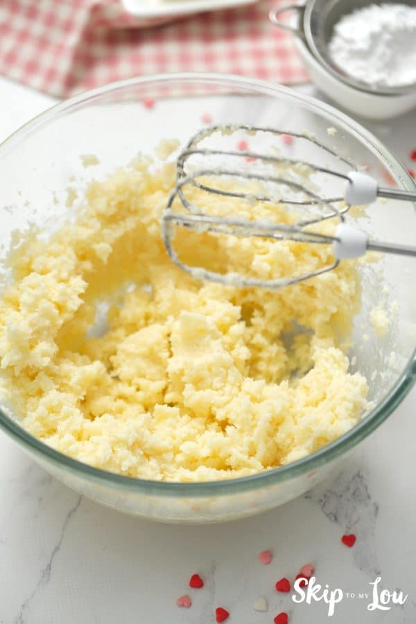 Clear glass mixing bowl with beaters and a sugar and butter mixture whipped up inside, by Skip to my Lou.