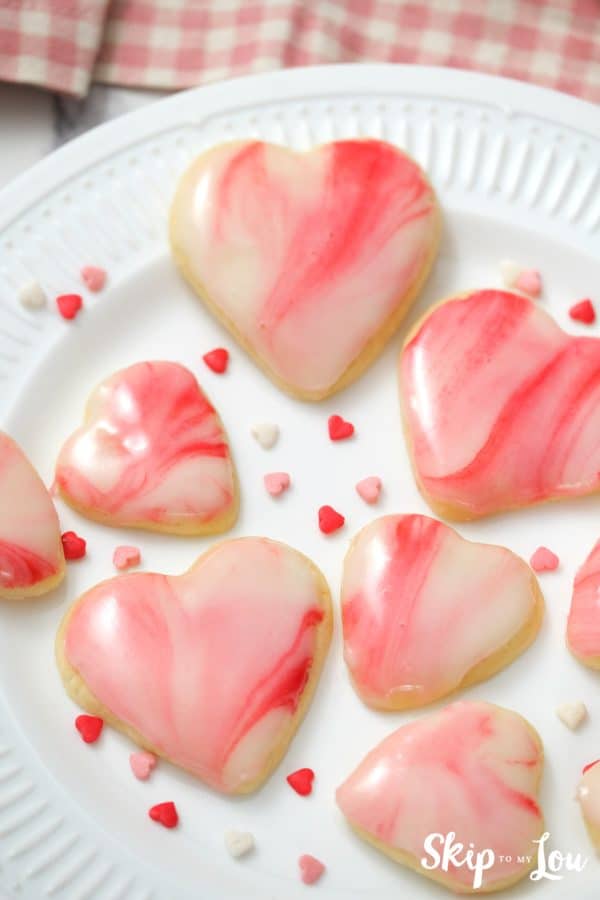 7 heart shaped sugar cookies with white, pink and red marbled icing on top, by Skip to my Lou.
