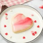heart shaped marbled sugar cookie on a white plate with scattered heart shaped sprinkles