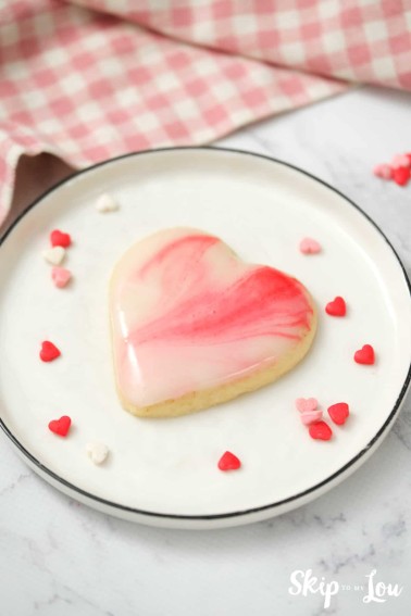heart shaped marbled sugar cookie on a white plate with scattered heart shaped sprinkles