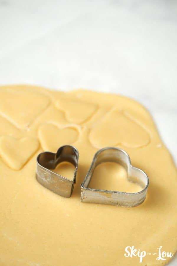 Two heart-shaped cookie cutters sitting on top of a slab of rolled out cookie dough, by Skip to my Lou.