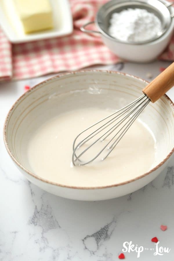 White ceramic mixing bowl with whisk and confectioner's sugar icing inside, by Skip to my Lou.