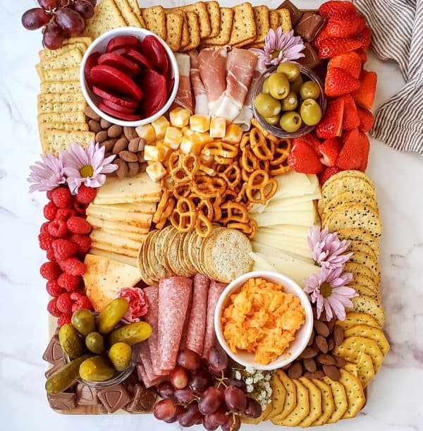 A traditional meat charcuterie board idea with crackers, bowls of pickles, olives, and cheese spread from Nellie Bellie's