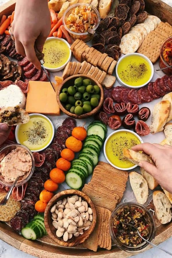 The Reluctant Entertainer with a large board that includes veggies, dips, meat, and cheese.