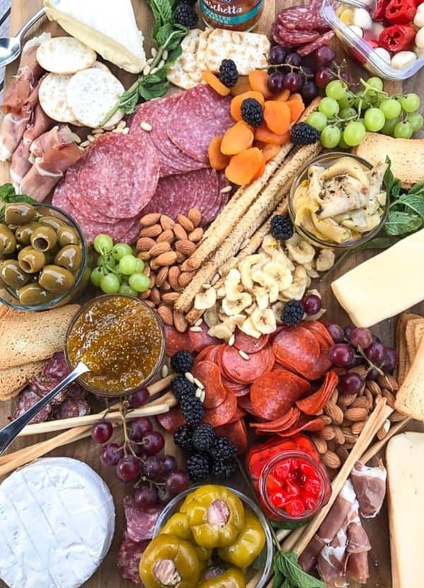 A large charcuterie board with different options like olives, pepperoni, nuts, dried bananas, cheese, and crackers from Skinny Taste.
