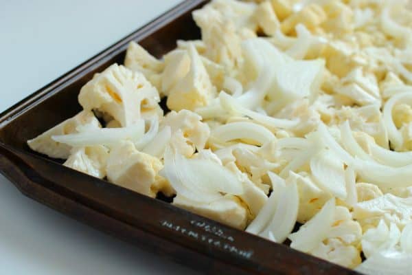 On a black roasting pan, florets of cauliflower and sliced onions ready to roast, by Skip to my Lou.
