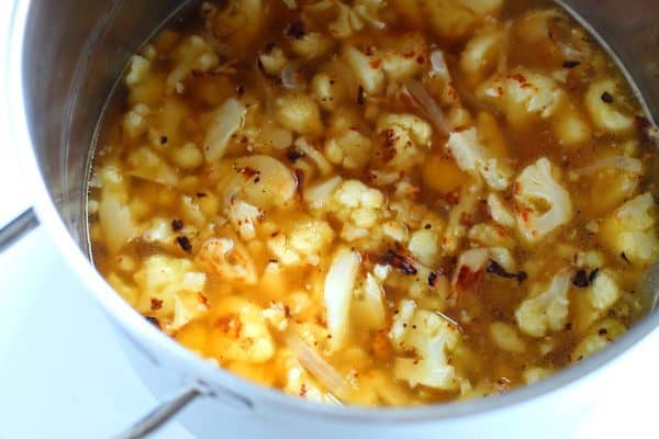 Roasted cauliflower, onions, and vegetable broth cooking inside a silver soup pot, by Skip to my Lou.