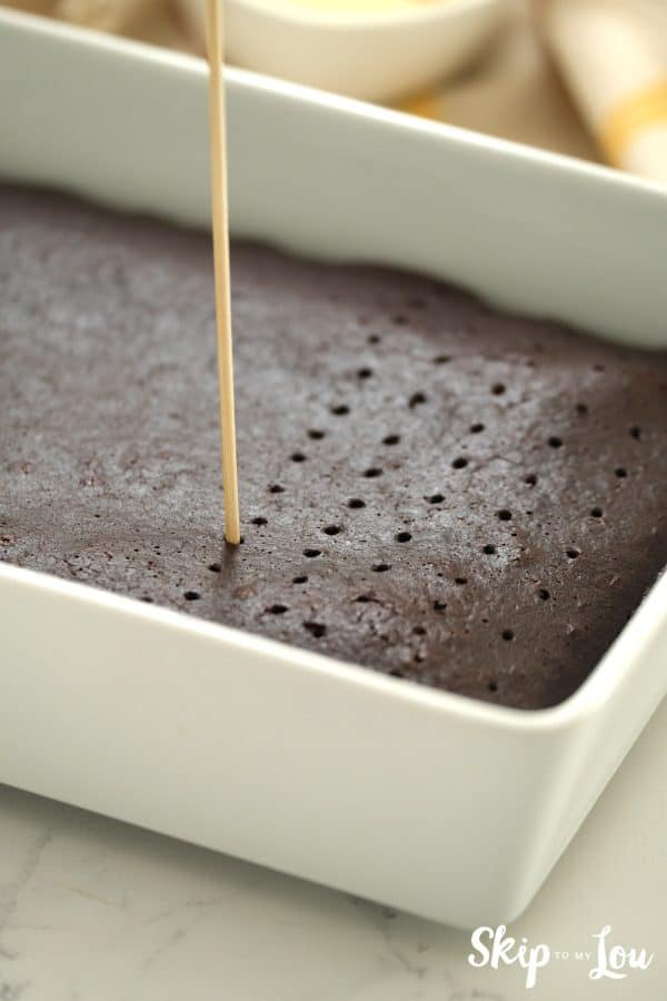 Wooden skewer poking rows of holes in the top of a chocolate cake, by Skip to my Lou. 
