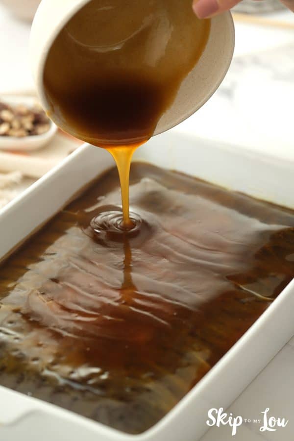 Caramel sauce pouring over the top of a chocolate cake baked in a rectangle-shaped pan, by Skip to my Lou.