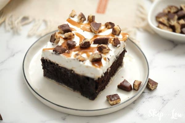 Serving of chocolate cake topped with whipped topping, caramel sauce and chocolate covered toffee bits, by Skip to my Lou.