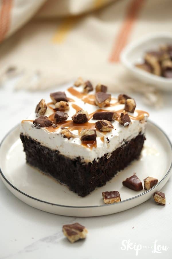 Serving of chocolate cake with whipped topping, caramel sauce and chocolate covered toffee bits, by Skip to my Lou.
