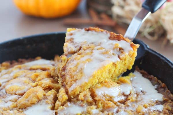 Pie shaped slice of pumpkin cinnamon roll skillet cake being lifted out of a black cast iron skillet with a spatula, by Skip to my Lou.