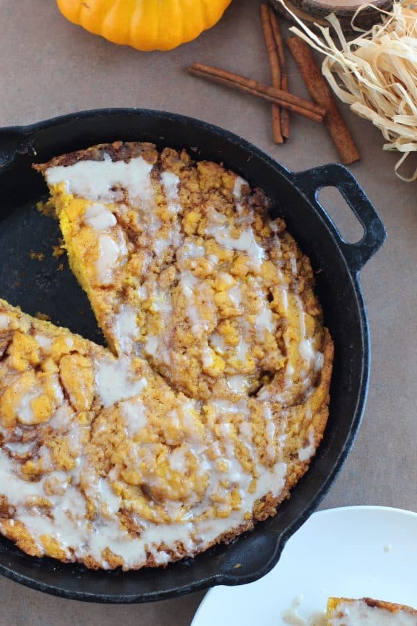 One slice missing from a pumpkin cinnamon roll skillet cake baked in a cast iron skillet, by Skip to my Lou.