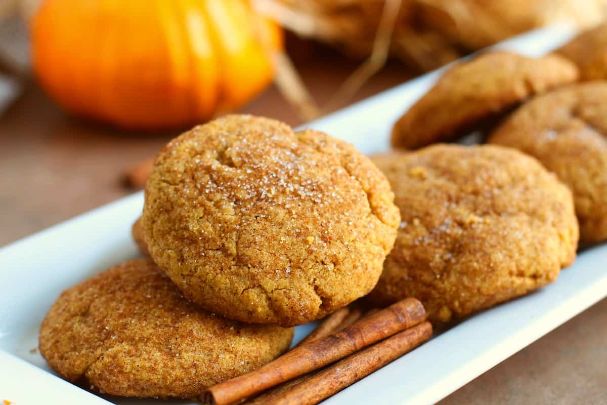5 pumpkin cookies and 3 cinnamon sticks sitting on a white rectangular tray, by Skip to my Lou.