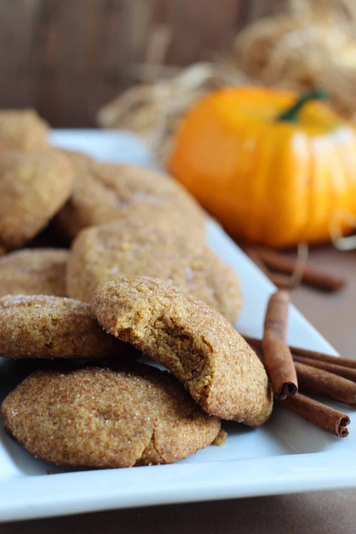 8 pumpkin cookies and 4 cinnamon sticks on a white tray, by Skip to my Lou.
