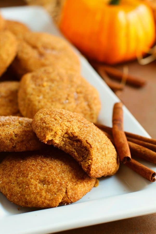 5 pumpkin cookies and 4 cinnamon sticks on a white rectangular tray, by Skip to my Lou.
