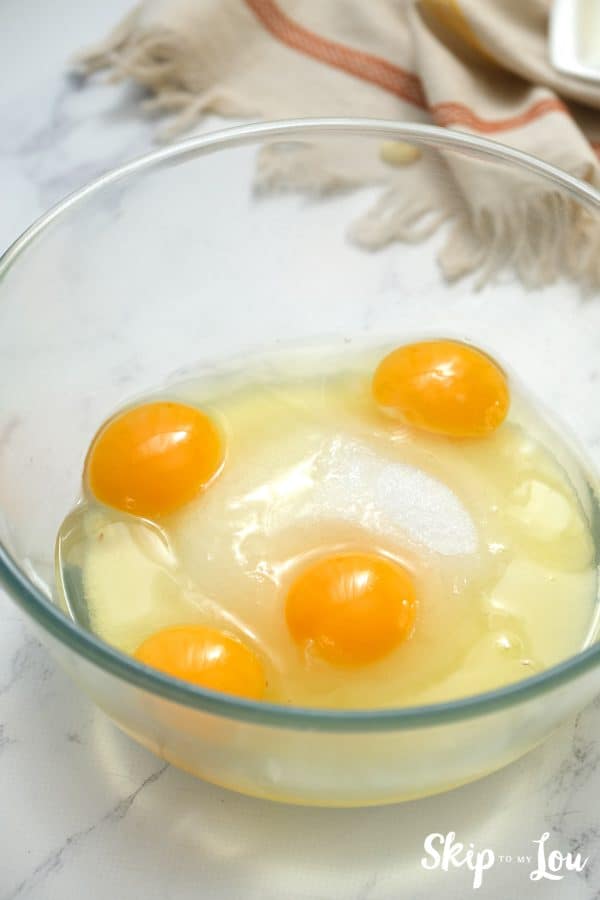 Glass bowl with sugar and four eggs cracked inside, by Skip to my Lou.