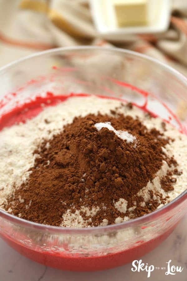 Glass mixing bowl with Red Velvet brownie mix, flour and cocoa powder inside, by Skip to my Lou.
