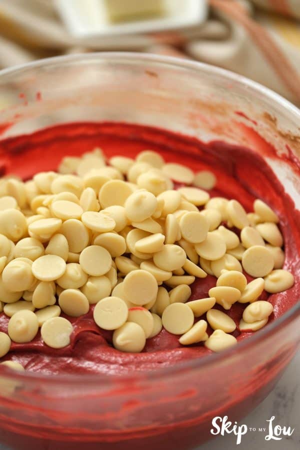 Glass bowl with Red Velvet brownie batter inside and white chocolate chips on top, by Skip to my Lou.