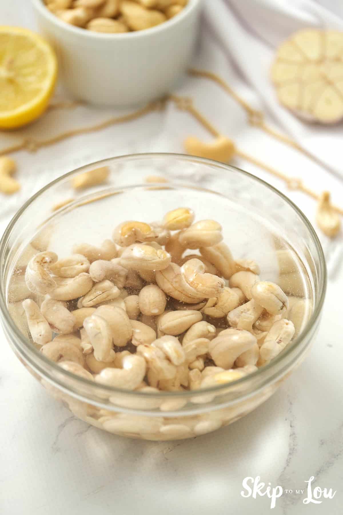 Raw cashews soaked in water in a glass bowl, by Skip to my Lou.