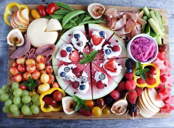 fruit charcuterie board ideas-windy city dinner fairy-board with a variety of fruits including half a watermelon with whipped cream on top, grapes, strawberries and a dip
