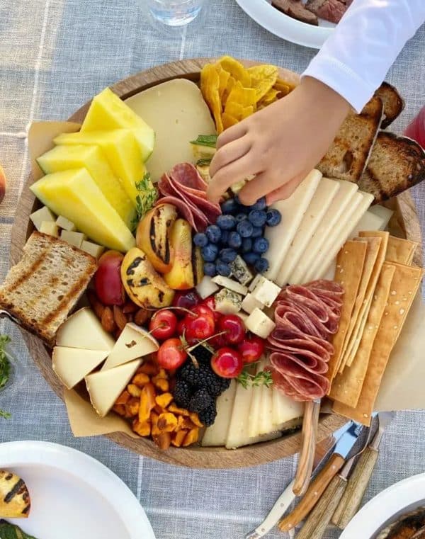 A board full of crackers, cheese, and some unique fruits from hip foodie mom