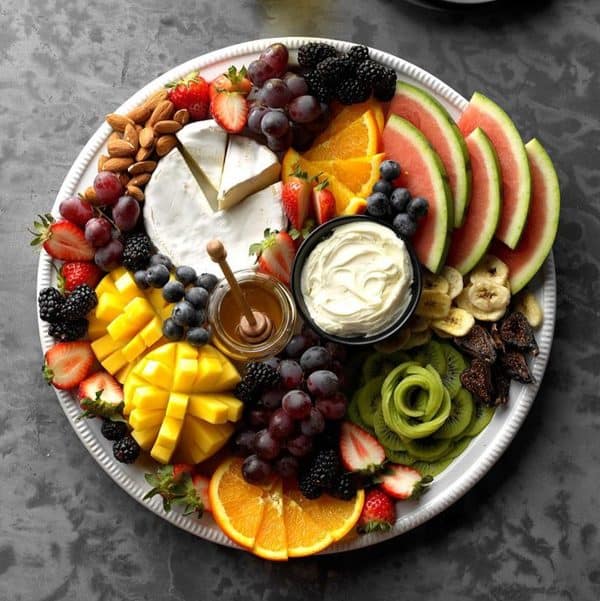 taste of home with cut up mango, kiwi shaped like a rose, and some cheese and honey options.