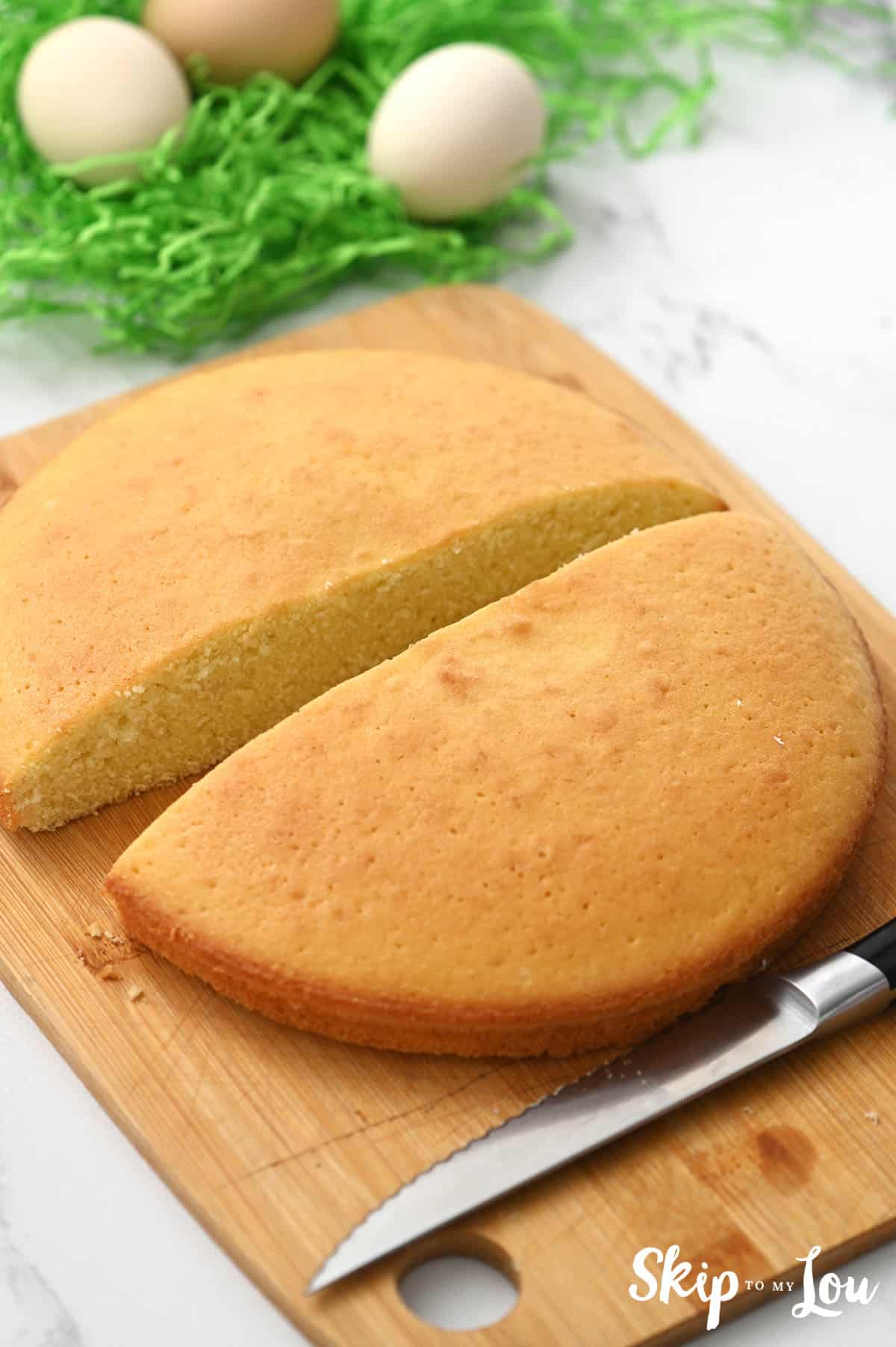 One round cake layer, sliced in half, sitting on a wooden cutting board with a serrated knife, by Skip to my Lou.