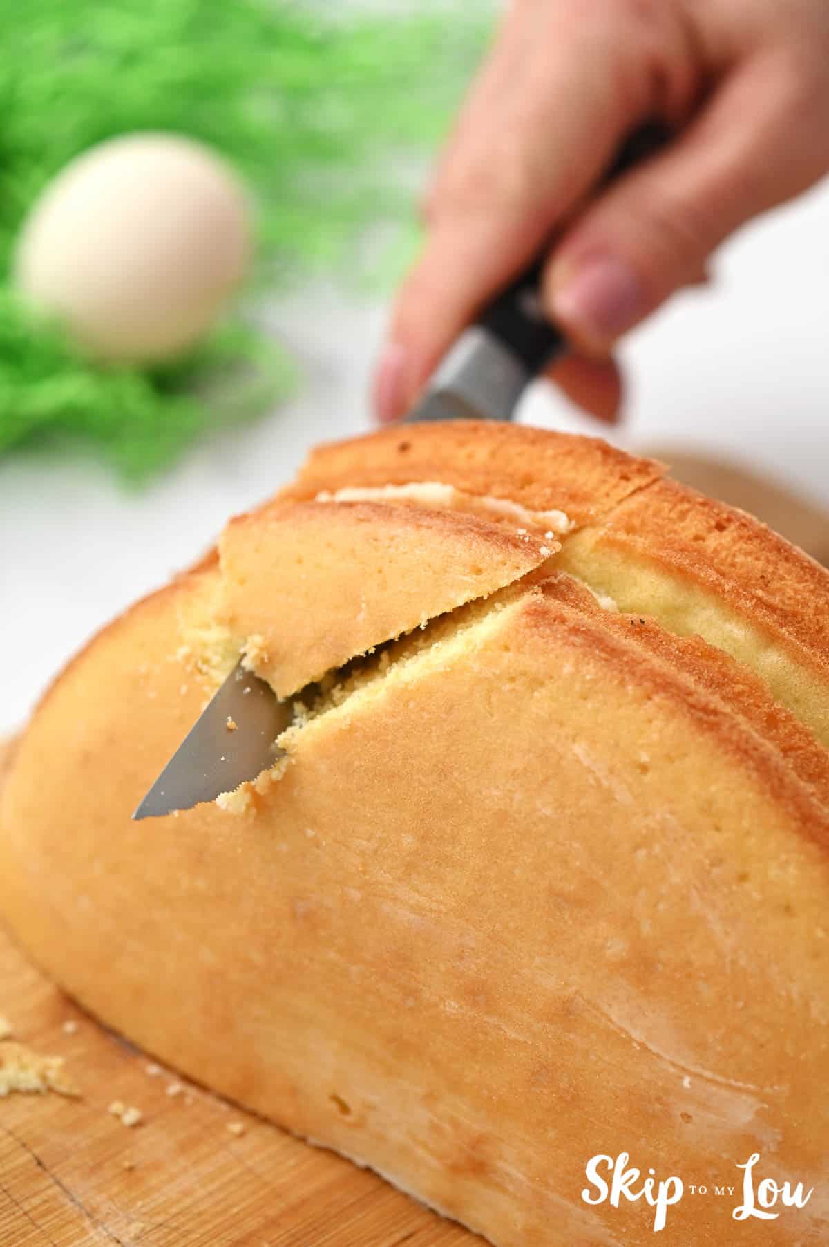 A serrated knife cutting a triangular section from cake layers frosted together and standing upright, by Skip to my Lou.