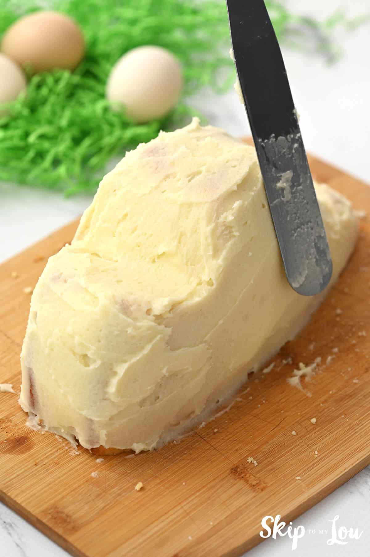 Offset spatula frosting a bunny cake with white frosting, by Skip to my Lou.