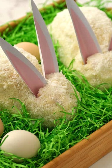 Two white Easter bunny cakes sitting on green Easter grass, by Skip to my Lou.