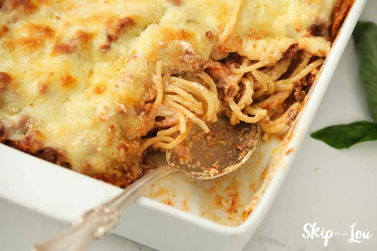 Silver serving spoon sitting in an Alfredo Spaghetti casserole with one serving removed, by Skip to my Lou.