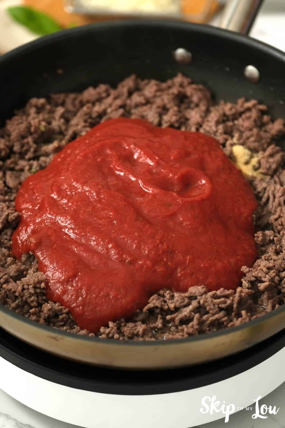 Ground beef browning in a skillet with red sauce on top, by Skip to my Lou.