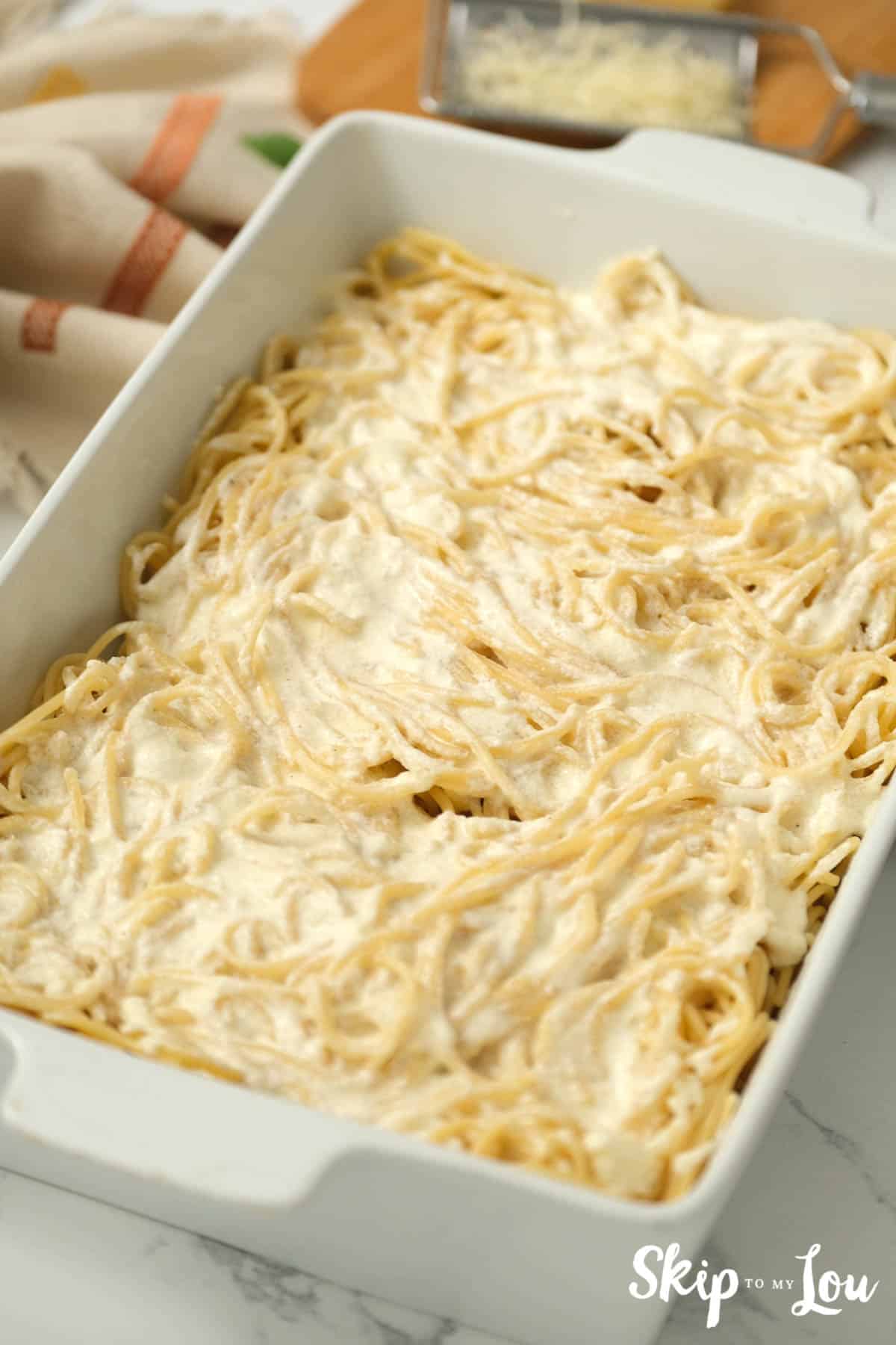 Alfredo sauce covering cooked spaghetti in a white casserole dish, by Skip to my Lou.