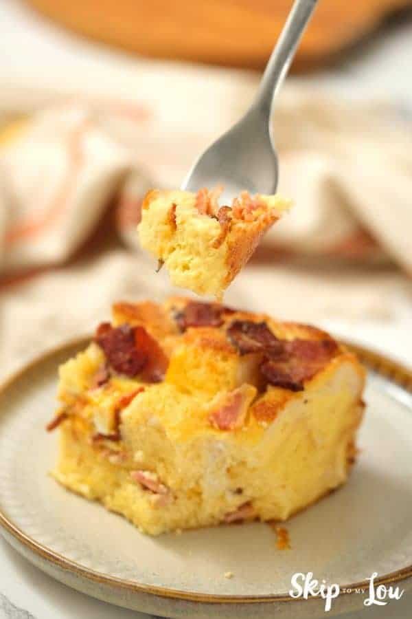 fork holding bite of egg strata from Skip to my Lou recipe over a serving of egg strata on a dish.