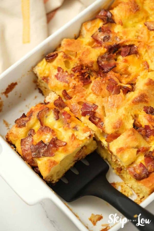 egg strata from Skip to My Lou recipe in a casserole dish with a serving getting scooped by a spatula.
