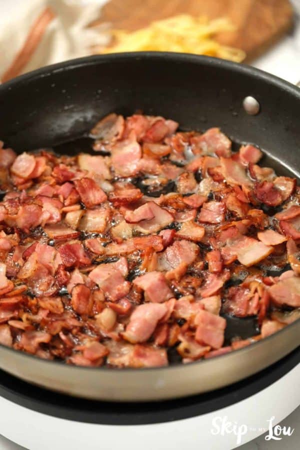 chopped bacon sizzling in a pan for egg strata from Skip to My Lou recipe