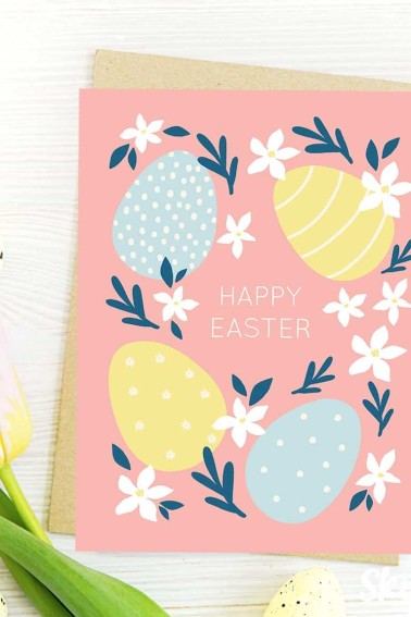 Image shows a pink Happy Easter greeting card decorated with Easter eggs and flowers, next to a white flower. from skip to my lou