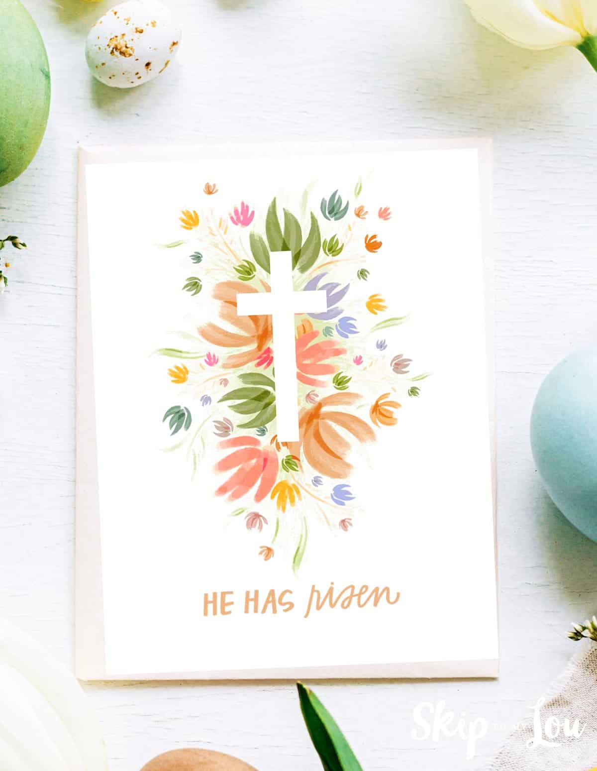 Image shows a Happy Easter he has risen greeting card with a colorful cross in the middle and surrounded by Easter decoration.