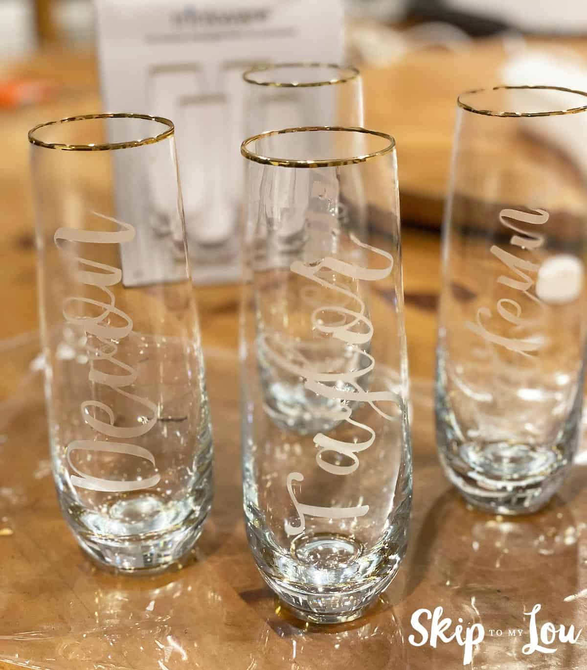 Personalized with names, 4 etched glasses sitting on a table, by Skip to my Lou.